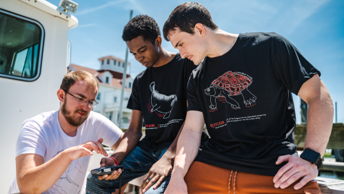 Rutgers Marine Field Station laboratory technician Douglas Hood (left) shows Jamin Brako (SOE '25; center) and Salvatore Fricano (SEBS '23) how to use equipment on the research boat.