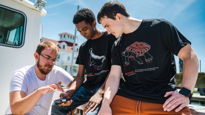 Rutgers Marine Field Station laboratory technician Douglas Hood (left) shows Jamin Brako (SOE '25; center) and Salvatore Fricano (SEBS '23) how to use equipment on the research boat.