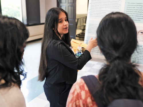 A student presenting her research poster to a group of other students