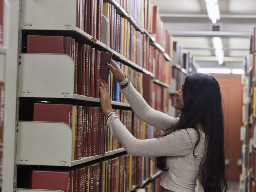 A student reaching for a book on a shelf in Alexander Library